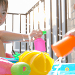 Japanese children play with water guns, floats, and other toys in a plastic pool placed on an apartment balcony.